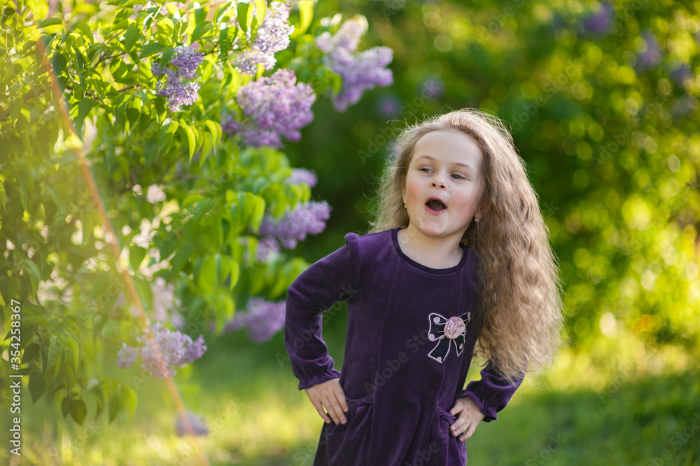 Outside portrait of a beautiful girl with long curly hair near lilac bushes Outside portrait of a beautiful girl with long curly hair near lilac bushes