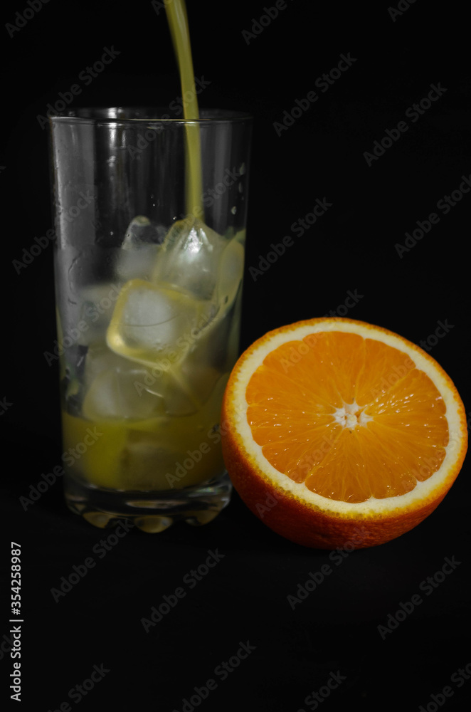 glass of freshly squeezed orange juice with ice on black background