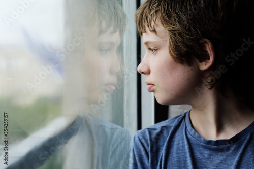 Cute 12 years old autistic boy looking through the window