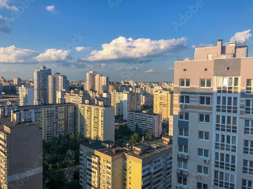 view from the top of the city on residential blocks of high rise buildings across blue sky and white clouds. Building infrastructure 
