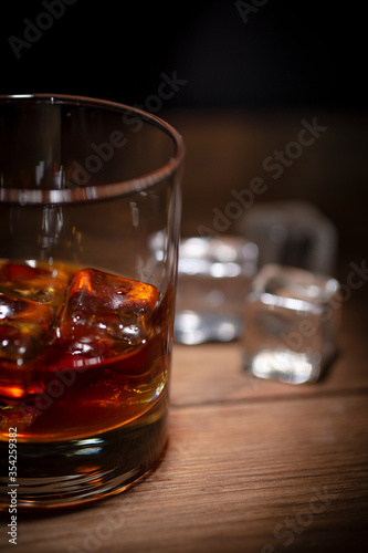 Fototapeta Naklejka Na Ścianę i Meble -  A glass of whisky with ice cubes on wooden background