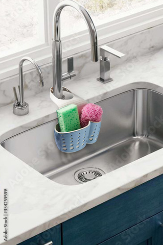 Detailed shot of a blue plastic sponge holder with an adjustable strap. The kitchen organizer with green and pink sponges is hanging on the chrome faucet over the kitchen sink. 