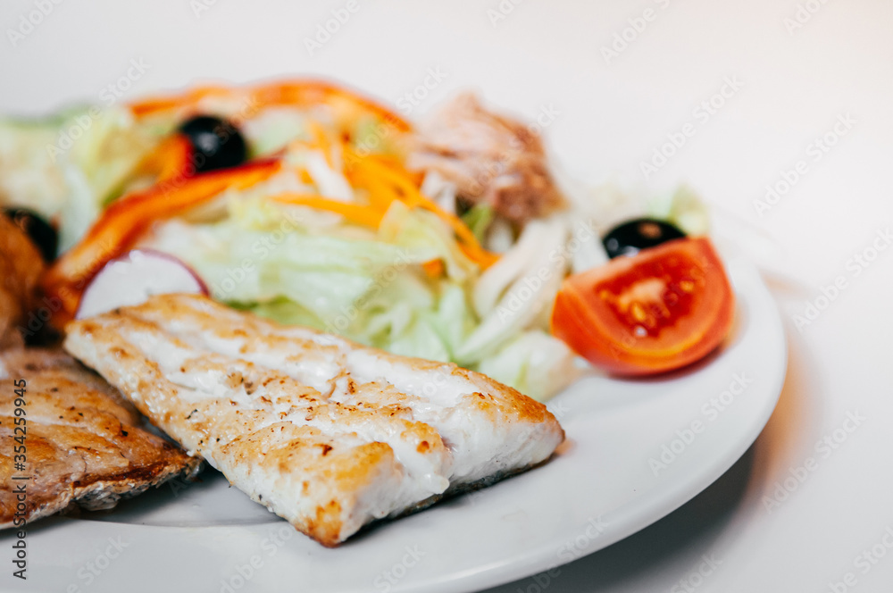 Sea bass fish steak golden grilled with fresh salad on white plate and white background Sea bass fish steak golden grilled with fresh salad on white plate and white background