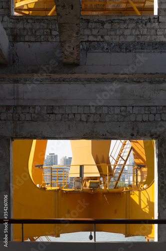 Fototapeta Naklejka Na Ścianę i Meble -  Yellow orange crane chassis in the sunny day. Brand new high lifter looking from the building around the river. The building along side the river in the background. Industrial machine and the building