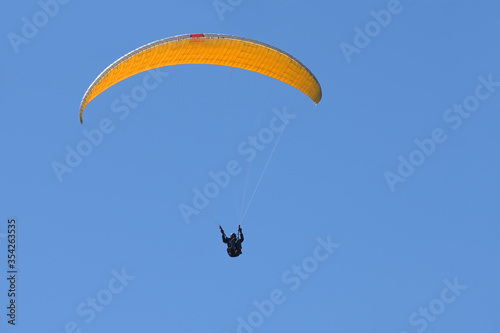 Paraglider pilot with an orange yellow glider is flying in the clear blue sky, recreational and competitive adventure sport, large copy space