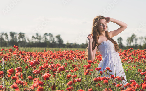 A girl in a white sundress enjoys the warmth of the sun and walks through a poppy field