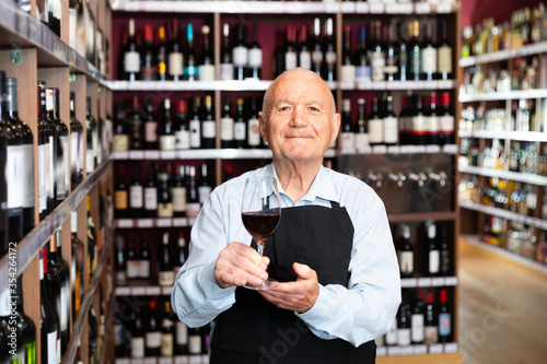 Successful elderly male owner of winery inviting to tasting wine of own production