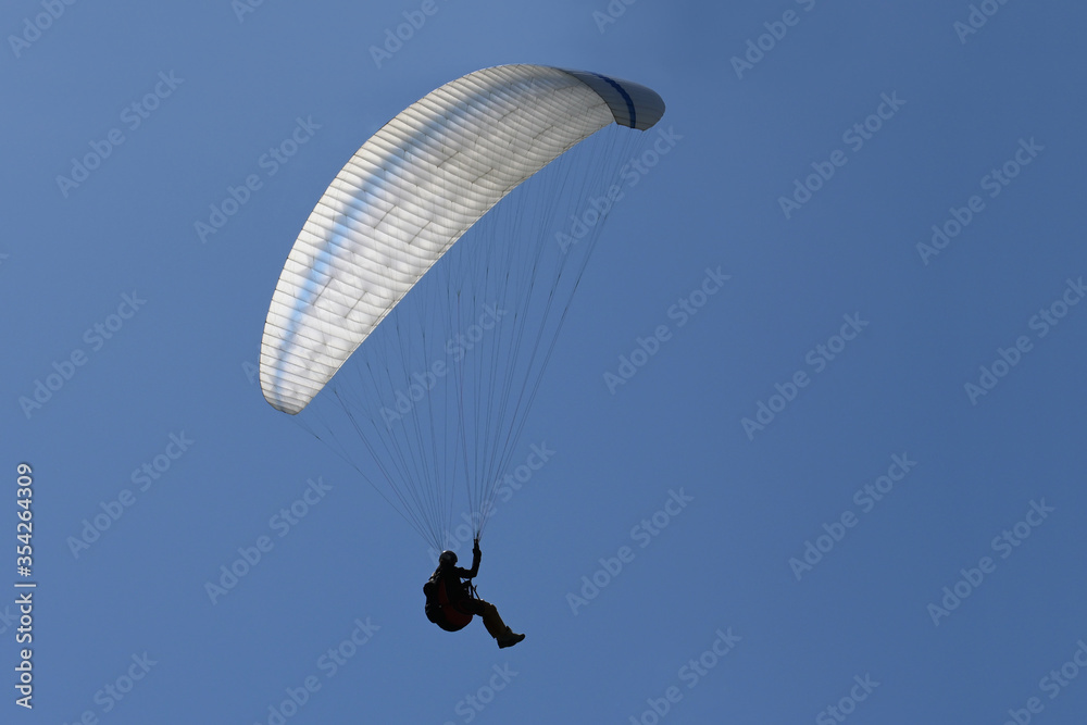 Paraglider pilot as silhouette with a white glider is flying in the clear blue sky, recreational and competitive adventure sport, copy space Paraglider pilot as silhouette with a white glider is flying in the clear blue sky, recreational and competitive adventure sport, copy space