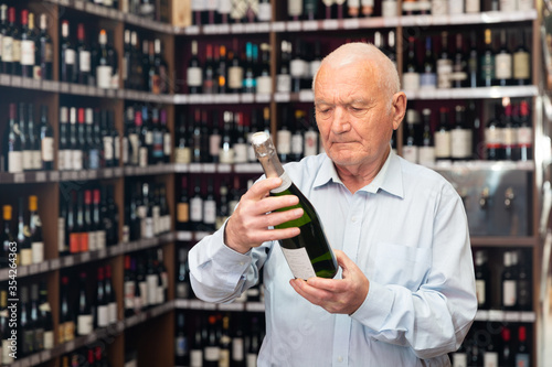 Attentive elderly man chooses champagne in a liquor store