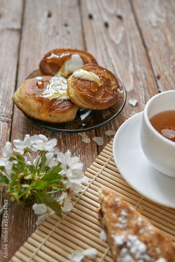 Pile of small homemade pancakes with honey, tea cup and honeycomb on wooden table