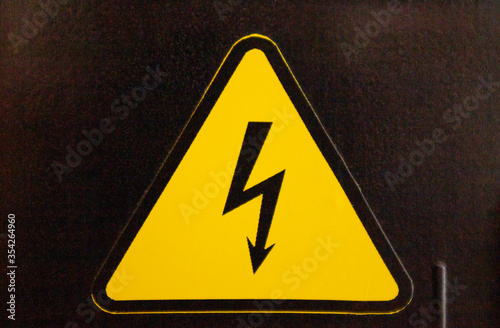 Yellow danger sign on a black wall. Black lightning in a yellow triangle.