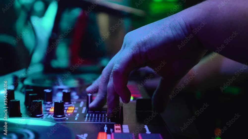 Hands DJ touching buttons sliders, playing electronic music on mixing deck, color illumination in nightclub dance party. Sound control console for mixing dance music and laptop in disco club. Hands DJ touching buttons sliders, playing electronic music on mixing deck, color illumination in nightclub dance party. Sound control console for mixing dance music and laptop in disco club.