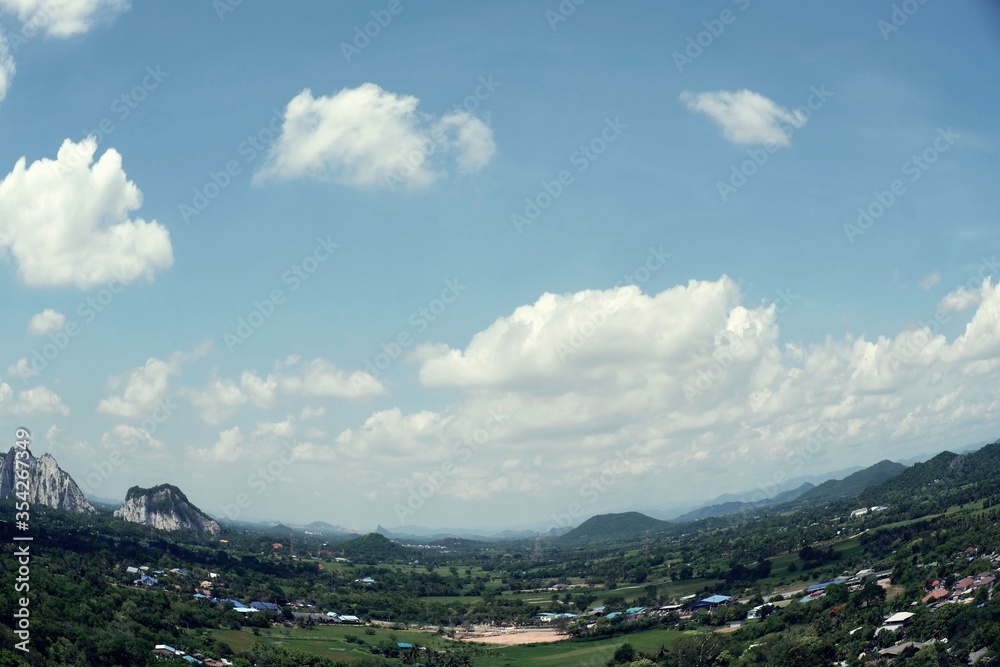 Residential buildings and green forest in aerial view. Landscape of village in the valley and beautiful blue sky with fluffy white clouds in a day.