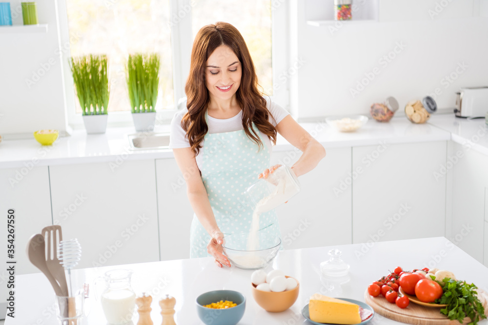 Portrait of charming positive housewife want prepare tasty pastry baked dessert pour flour in bowl wear apron in light house kitchen