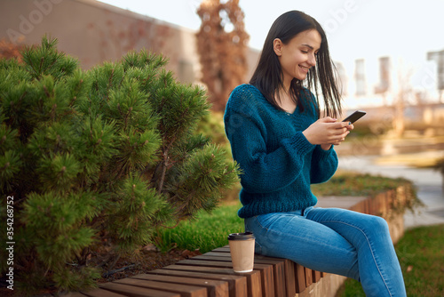 Charming female using mobile phone on a bench