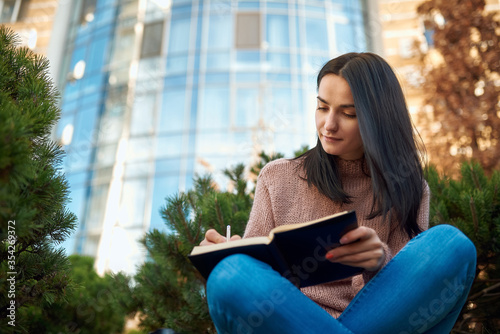 Lovely lady doing written work on a lawn in front of tall building