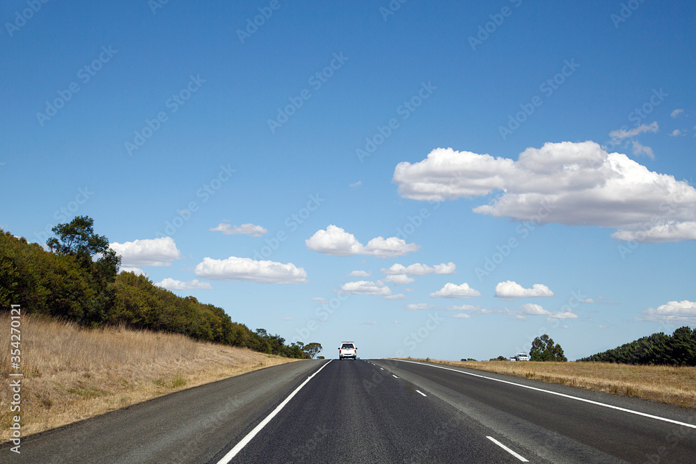 Following a white pick up truck on the highway in rural Victoria State - Australia. Blue sky with white clouds.