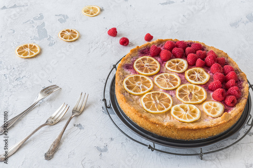 Cheese cake with raspberries and dried lemon slices on white background  some raspberries  lemon slices and three forks lying on the table.