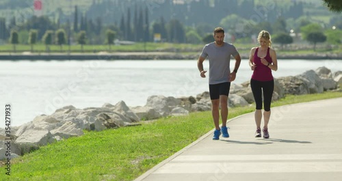 4K Slow Motion Of Active Couple Going For Jog Around Lake On Summer Day