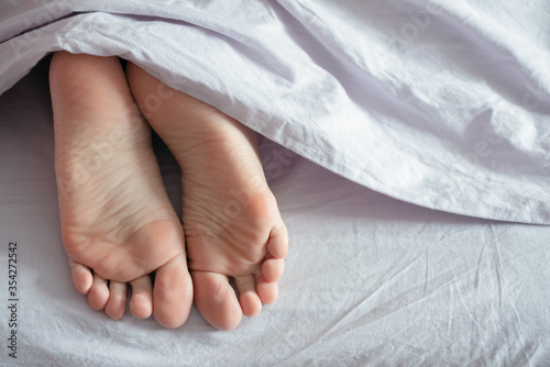 Female feet under a blanket close up.