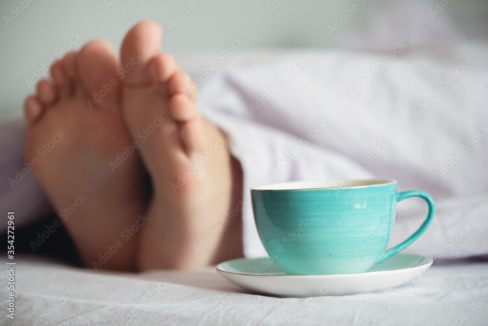 Cup of coffee or tea and female legs under a blanket close up. Woman morning.