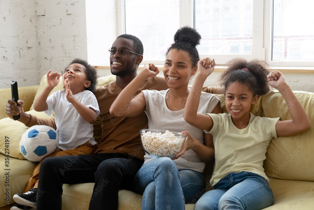 African couple and children football lovers fans enjoy favourite team game  sit on sofa eat popcorn celebrate goal, spend time together with small  kids. Pastime and hobby, happy family activity concept foto