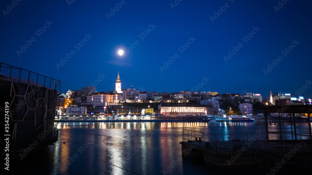 Night landscape of Belgrade from the bank of the river Sava, full moon in the sky above the city.