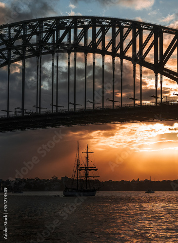 Sailing ship under the bridge in the city during sunset