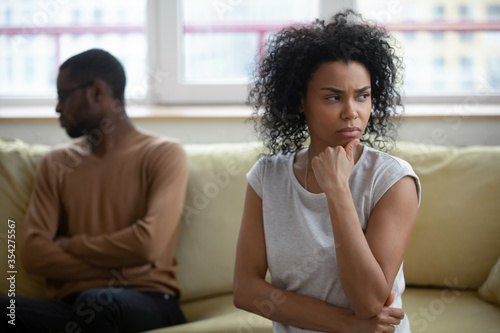 African wife looking dissatisfied sitting on sofa with husband apart, couple thinking about problems in relations, feels annoyed and unhappy. Break up relationships end, decision about divorce concept