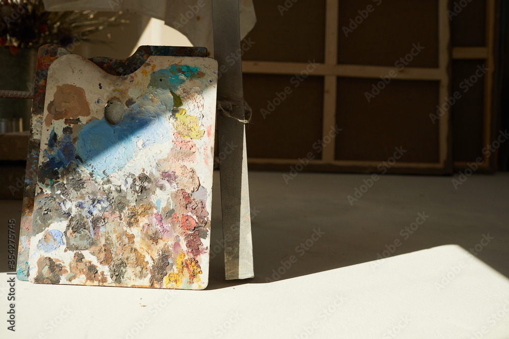 Background image of colorful artists palette lit by sunlight in empty art studio interior, copy space
