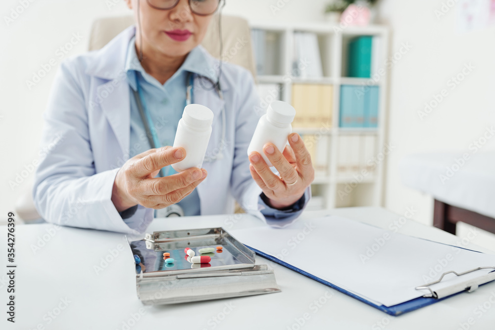 Cropped image of doctor reading information on small containers with pills and supplements