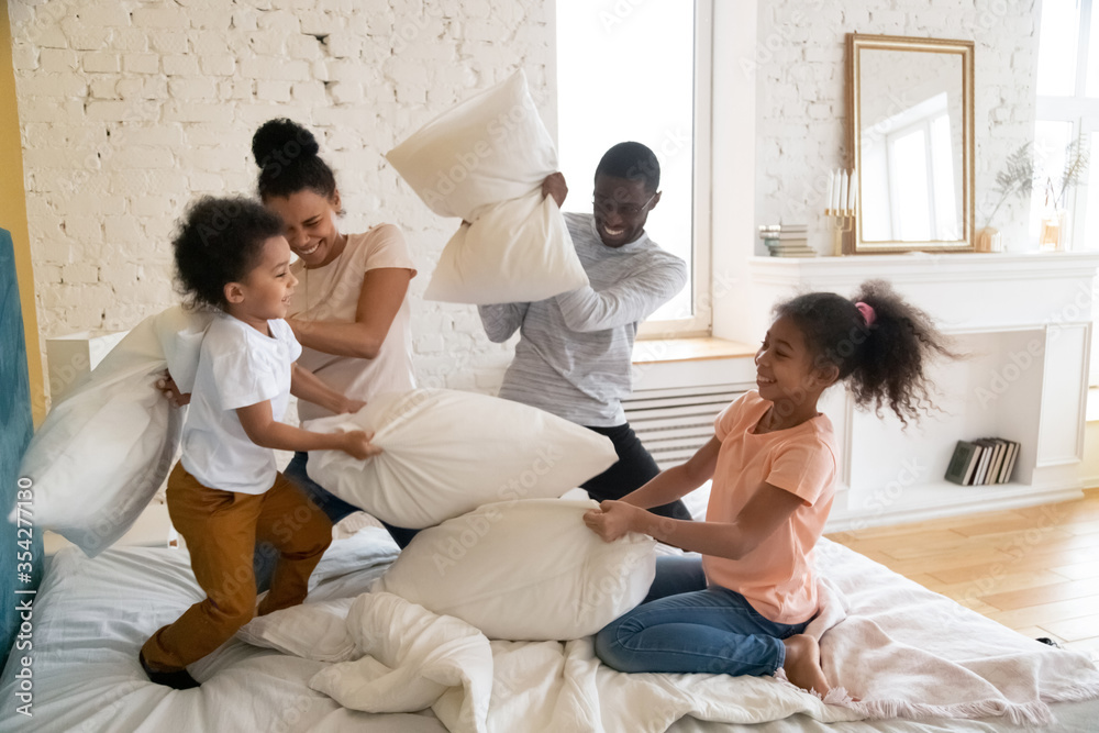 African family with pre-teen daughter and preschool son spend funny time in bedroom fighting with pillows moving on mattress on bed. Play active game with children, have fun at new modern home concept African family with pre-teen daughter and preschool son spend funny time in bedroom fighting with pillows moving on mattress on bed. Play active game with children, have fun at new modern home concept