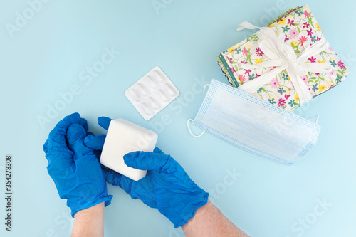 Person wearing blue nitrile surgical gloves holding soap and paracetamol. Image shows yellow clock wearing face mask, concept image showing safety precautions to take in current coronavirus pandemic 