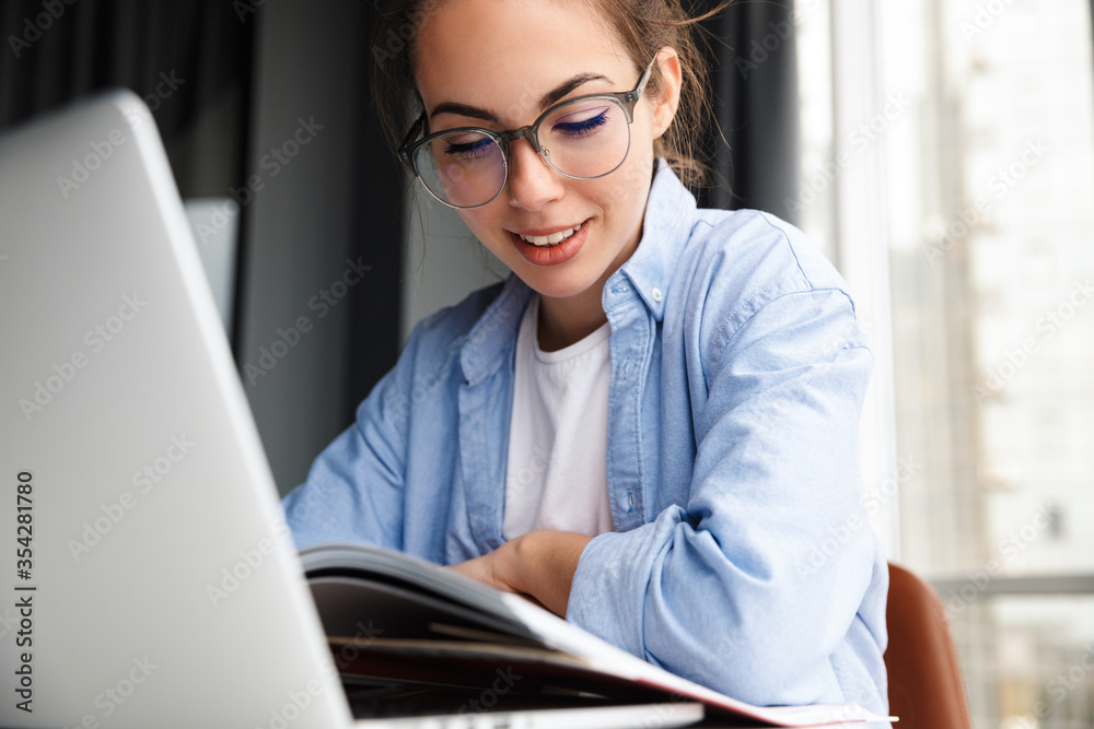 Image of woman reading book and working with laptop while sitting Image of woman reading book and working with laptop while sitting