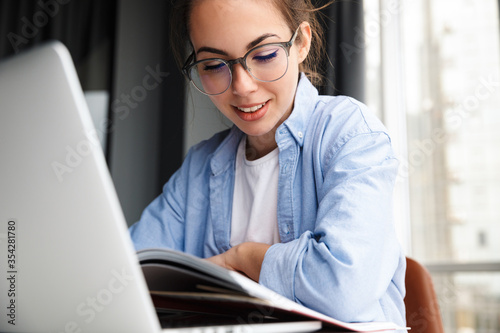 Image of woman reading book and working with laptop while sitting