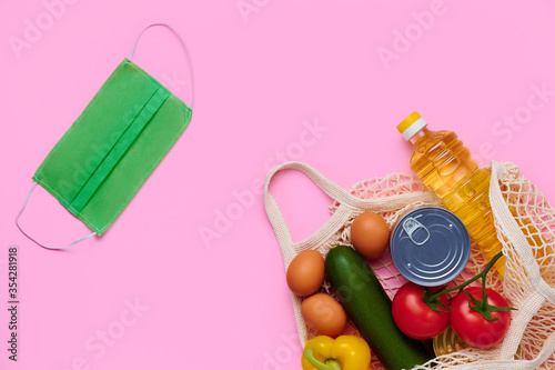 Donation food, fresh vegetables in the string bag. Chicken eggs, zucchini, tomatoes, sunflower oil, yellow fresh pepper, medical protective mask photo