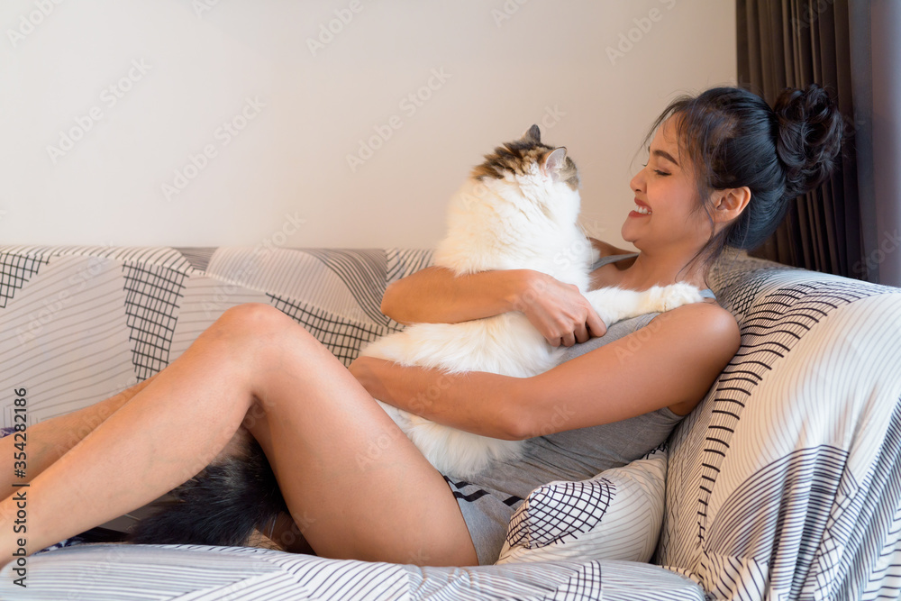 Naklejka premium Happy young beautiful Asian woman hugging Persian cat in the sofa at home
