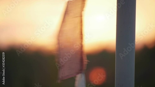 a Buddhist prayer flag flutters in the wind against the red setting sun