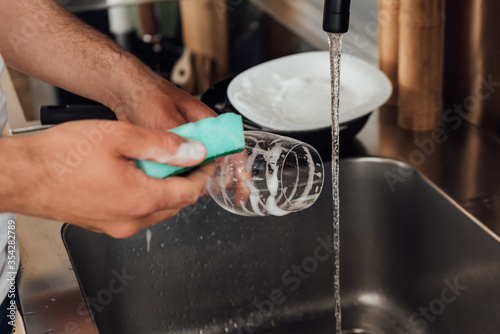 Cropped view of man cleaning wine glass with sponge in kitchen
