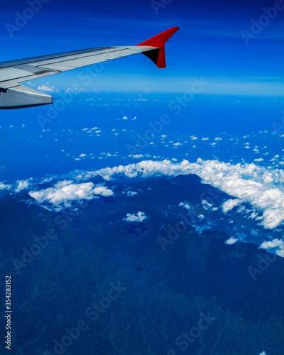 Mountain terrain landscape covered with some cloud on a blue sky day, bird eye view looking from an airplane.