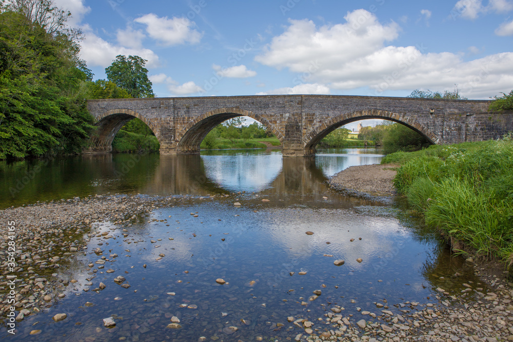 Large stone bridge crossing the river Ribble at Brungerley park, Clitheroe. Low water in summer exposing pebbles.