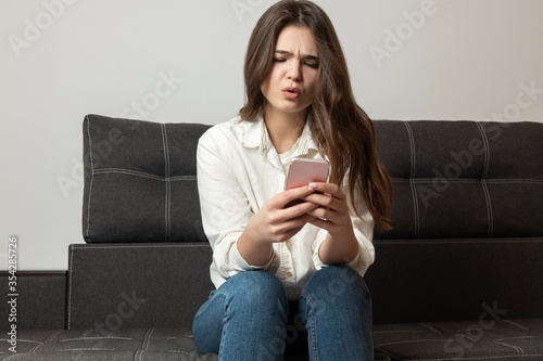 young beautiful brunette smiling womansitting on the sofa in her appartment looks amazed while replying to message in her smartphone, feeling cozy at home photo