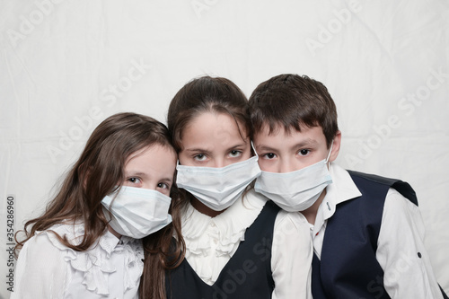 family of three little kids in medical masks and school uniform during coronavirus COVID-19 quarantine with copy space