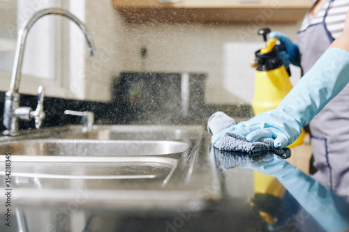 Close-up image of woman spraying disinfecting detergent on kitchen counter and sink to kill all bacteria