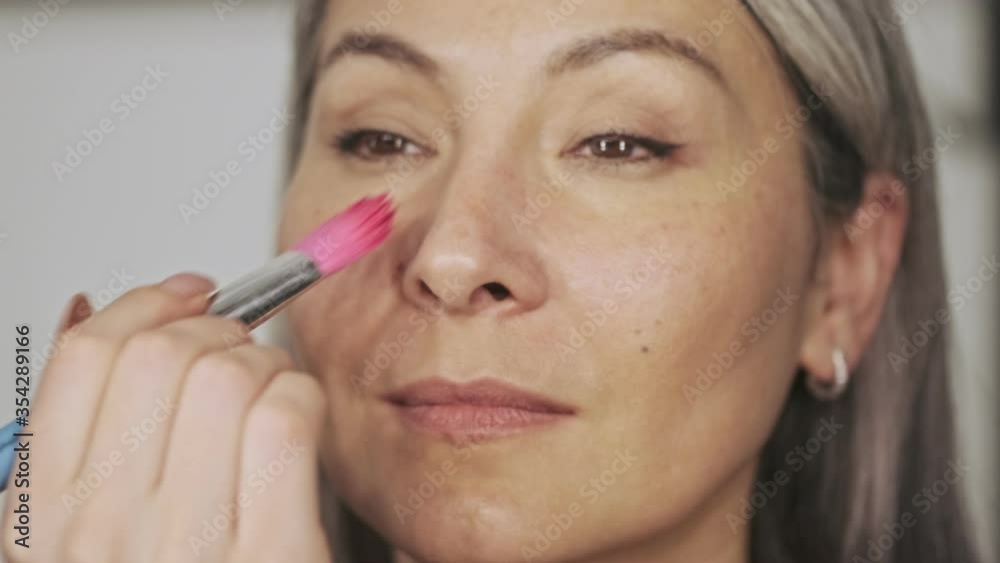 A close-up view of a happy elderly woman client is been doing makeup with a makeup artist in a beauty salon A close-up view of a happy elderly woman client is been doing makeup with a makeup artist in a beauty salon