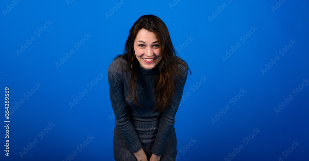 Photo of smiling, cheerful young female in grey dress on blue background Photo of smiling, cheerful young female in grey dress on blue background