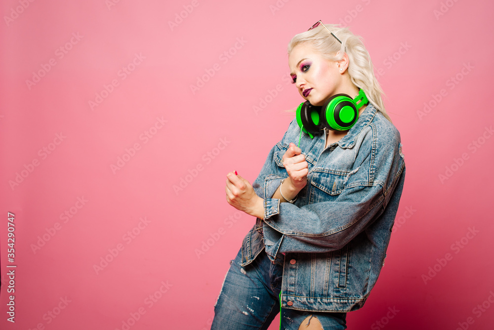 Happy stylish blond woman in pink glasses with big headphones listening music and dancing on colored background Happy stylish blond woman in pink glasses with big headphones listening music and dancing on colored background