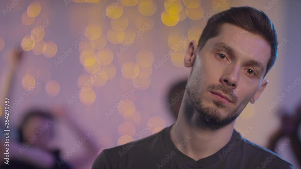 Slowmo tracking with close up of man with beard standing and looking at camera with bored expression as unrecognizable people partying in background Slowmo tracking with close up of man with beard standing and looking at camera with bored expression as unrecognizable people partying in background