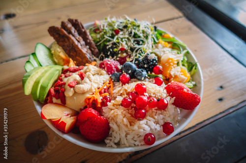 Delicious vegan food bowl with fresh fruits, avocado, salad and rice. Concepts of vegan food trend, healthy eating lifestyle, superfood cuisine. Closeup, side lit, horizontal format.