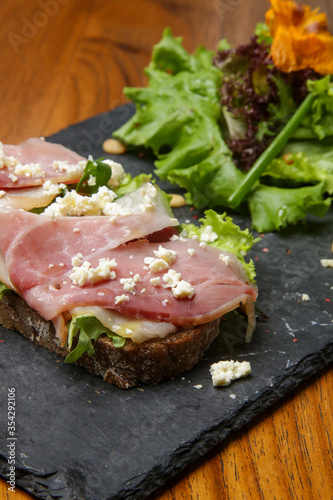 Open prosciutto cheese green salad sandwich on rye bread slices 